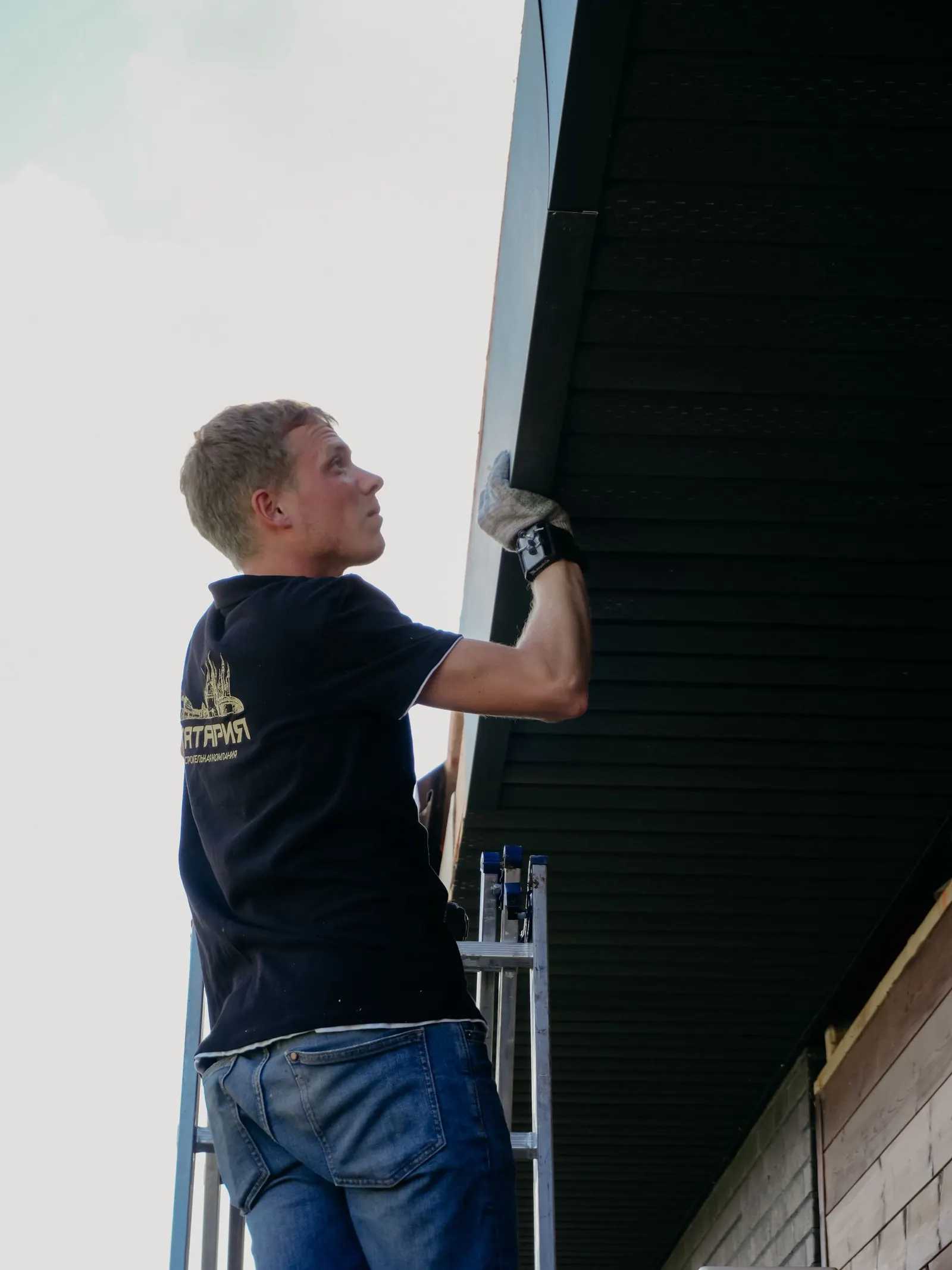 Worker on a ladder repairing the edge of a residential roof.
