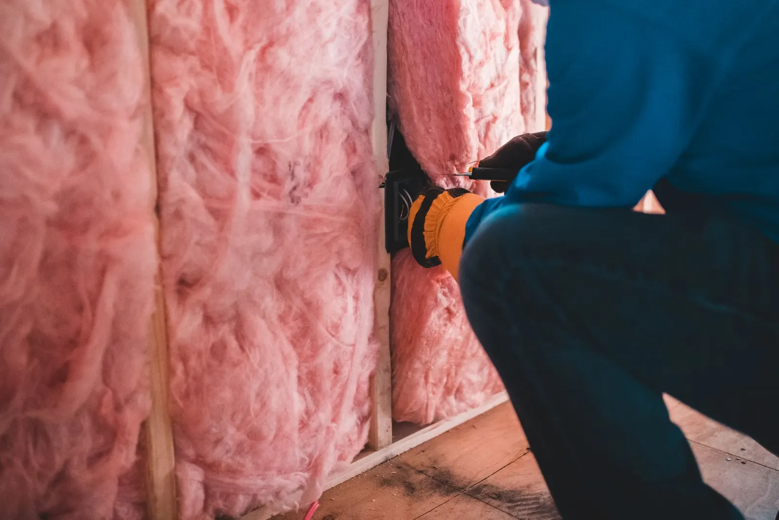 Gloved worker installing fiberglass insulation inside a building.