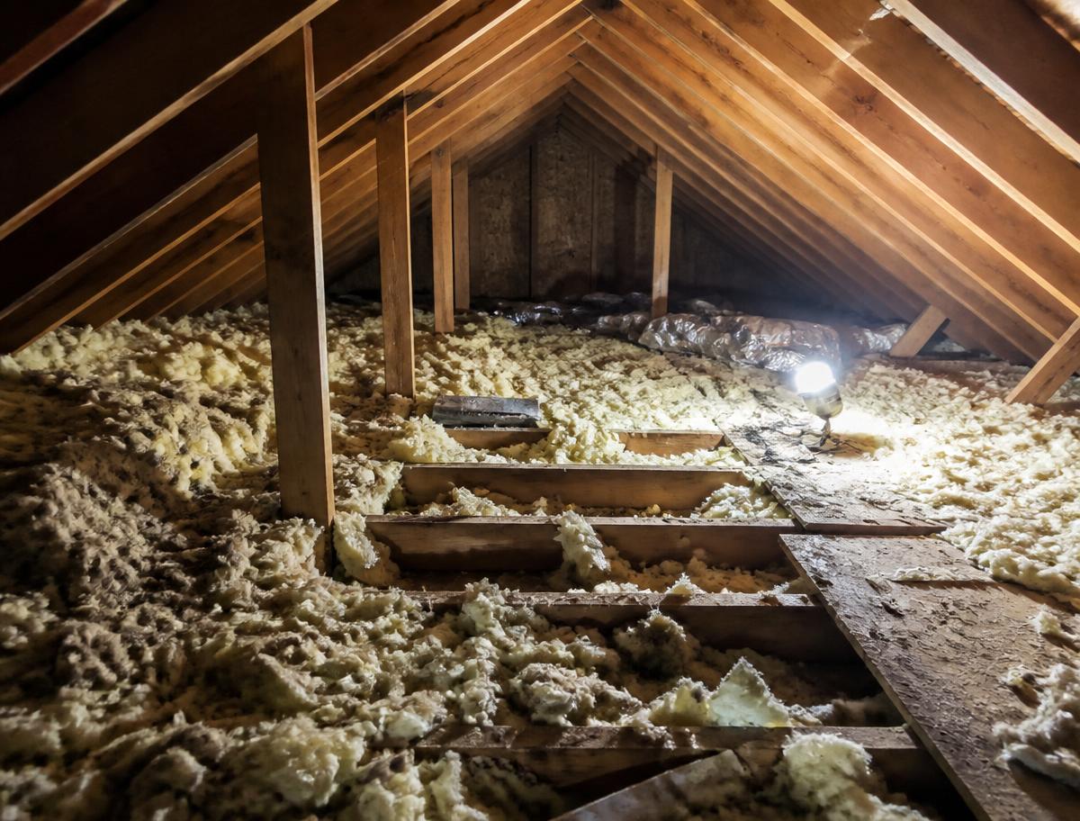 Residential attic interior with disturbed and damaged fiberglass insulation between rafters