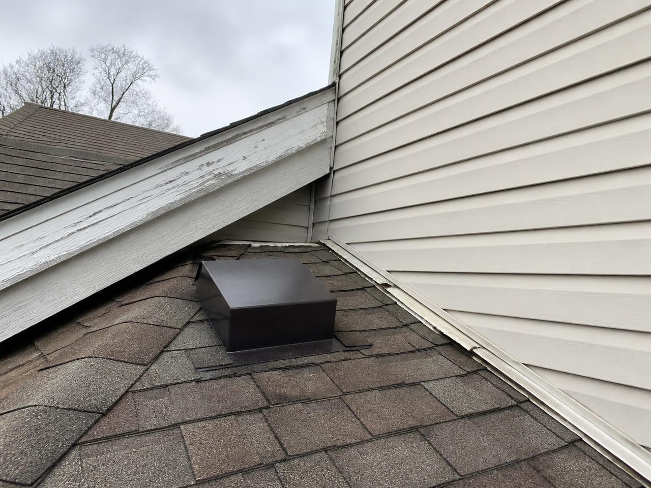 Roof vent and rake edge where an addition roof meets the siding of a residential home, with weathered trim and flashing