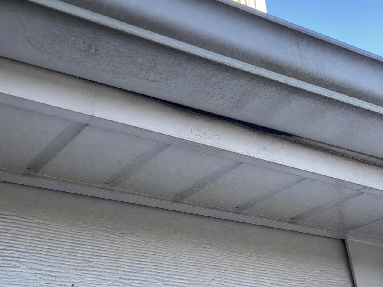 Close view of a weathered aluminum soffit panel separated slightly from the fascia board beneath a residential gutter