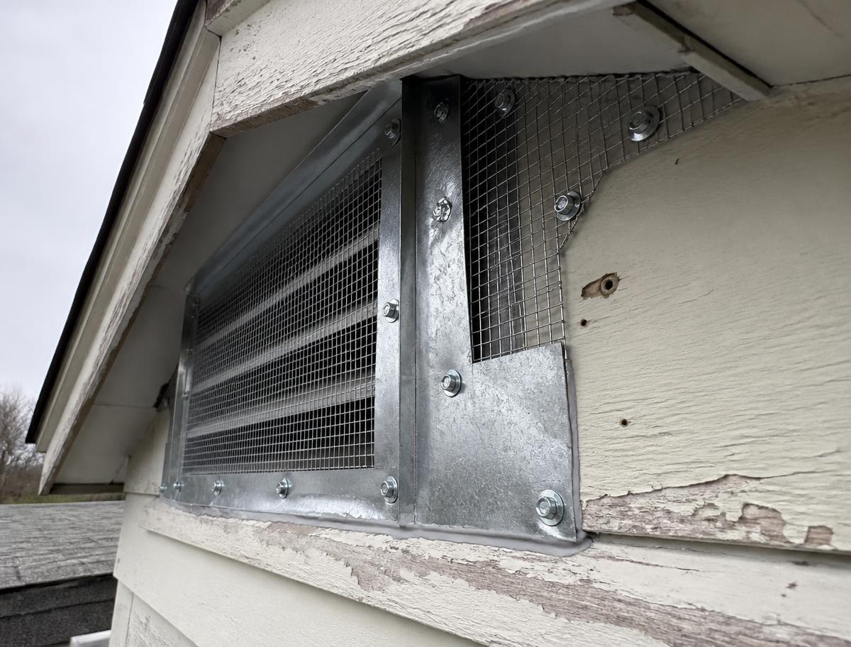 Steel mesh and metal flashing covering a roof vent opening on a house exterior