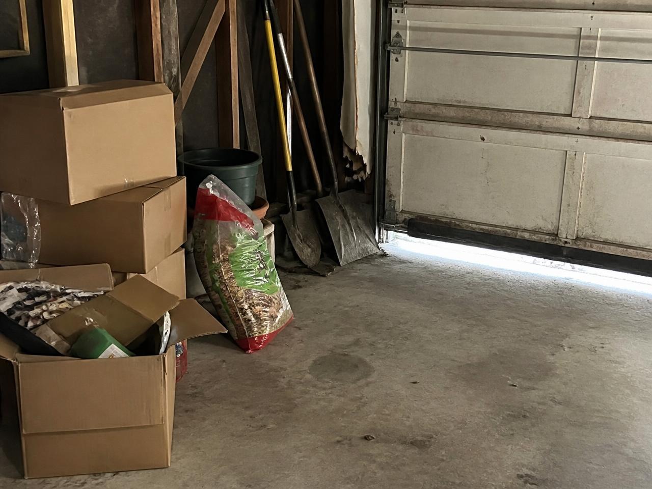 Interior corner of an attached residential garage with stored boxes and daylight showing under a worn garage door seal